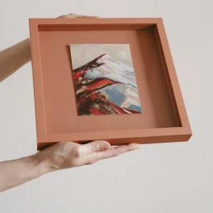 terracotta coloured square framed pastel study of a colourful mountain